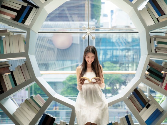 Asian girl reading on a bookshelf in a library in her university