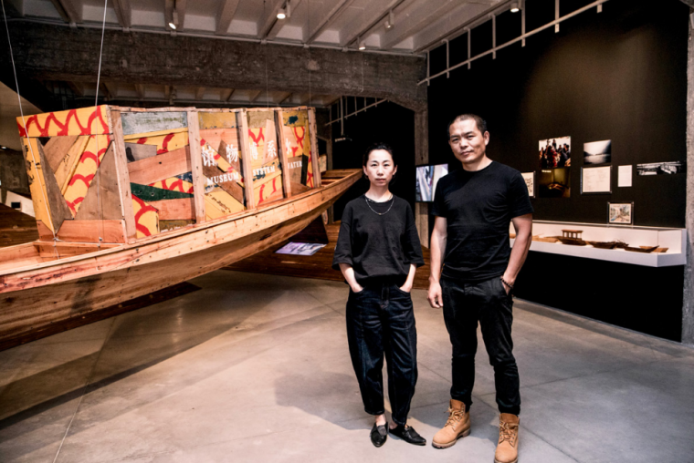 Picture of CAO Minghao & CHEN Jianjun in front of an art installation of a boat with boxes on it