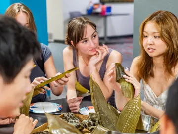 Campers sitting at table wrapping food in leaves